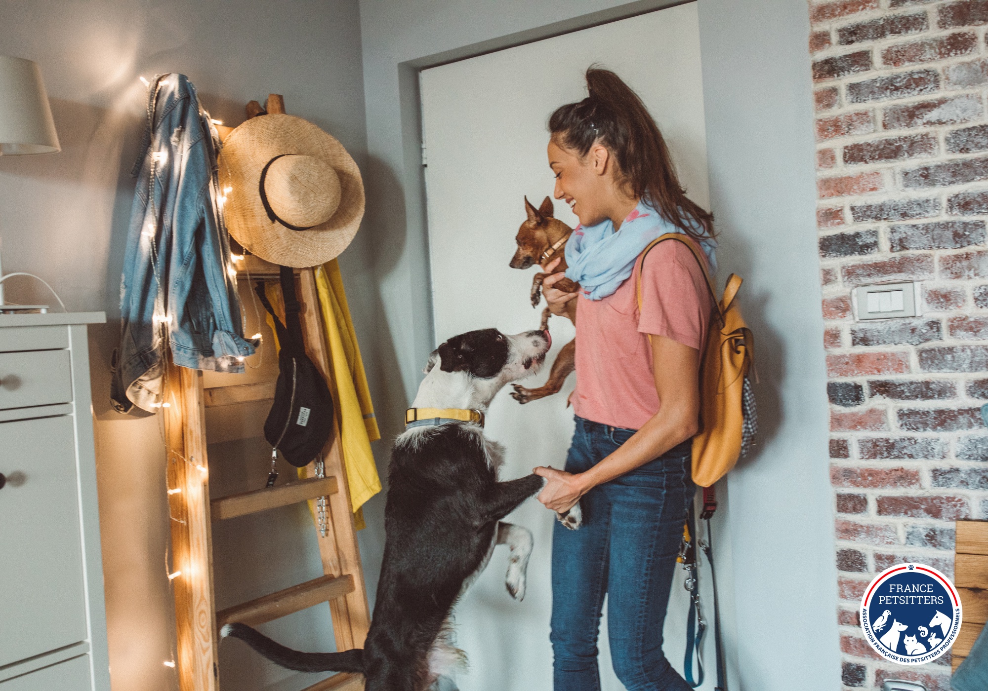 Une petsitter arrive chez un client, son sac à l’épaule, accueillie par deux chiens