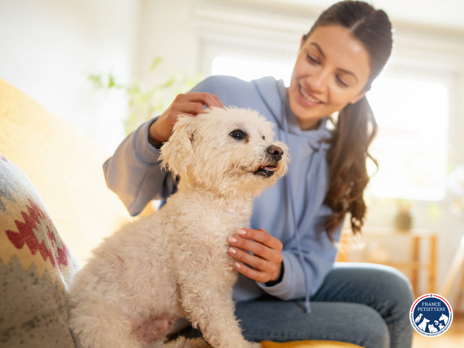 Une petsitter caresse un petit chien blanc sur un canapé